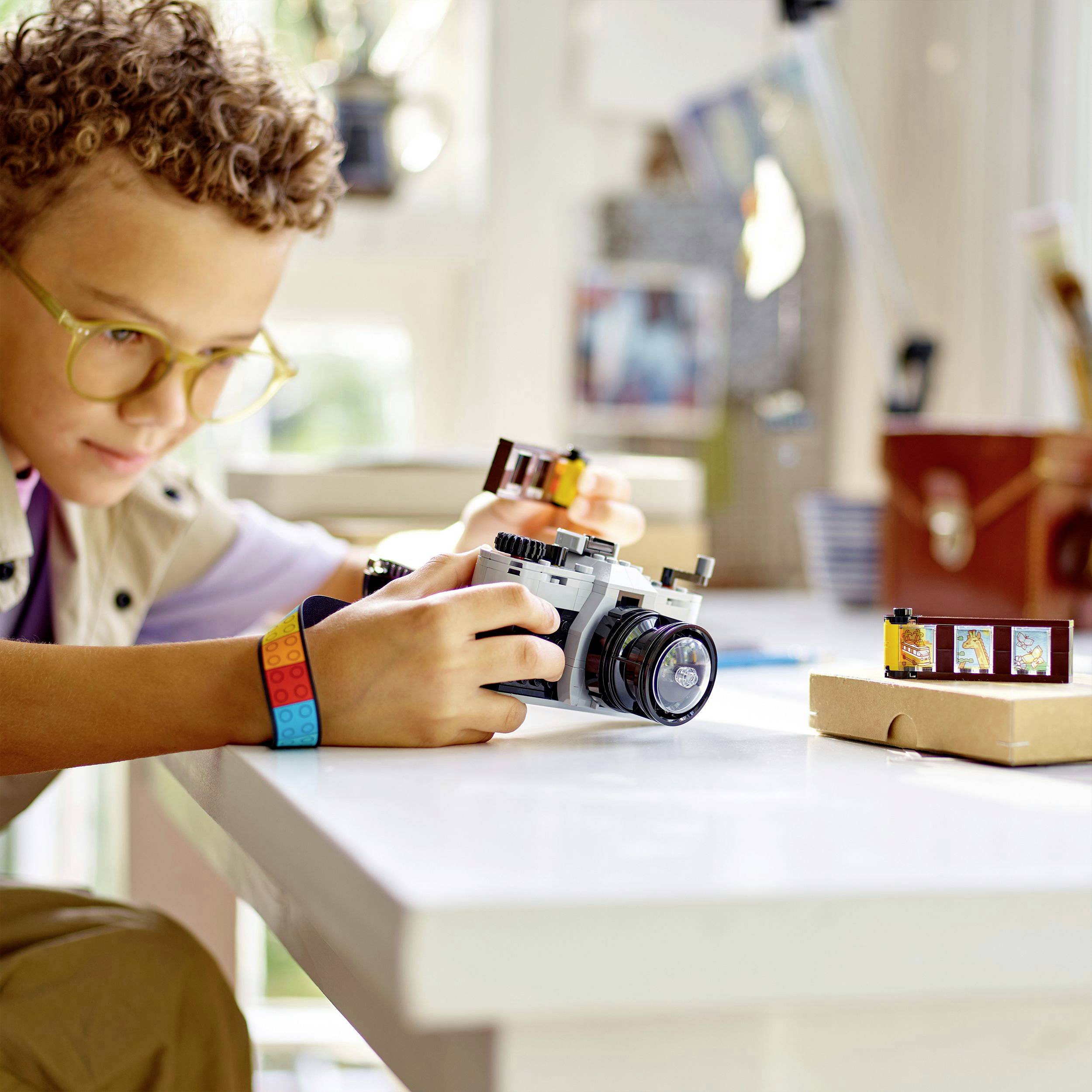A person is sitting at a table and constructing a camera out of building blocks. Additional small building blocks are scattered on the table.