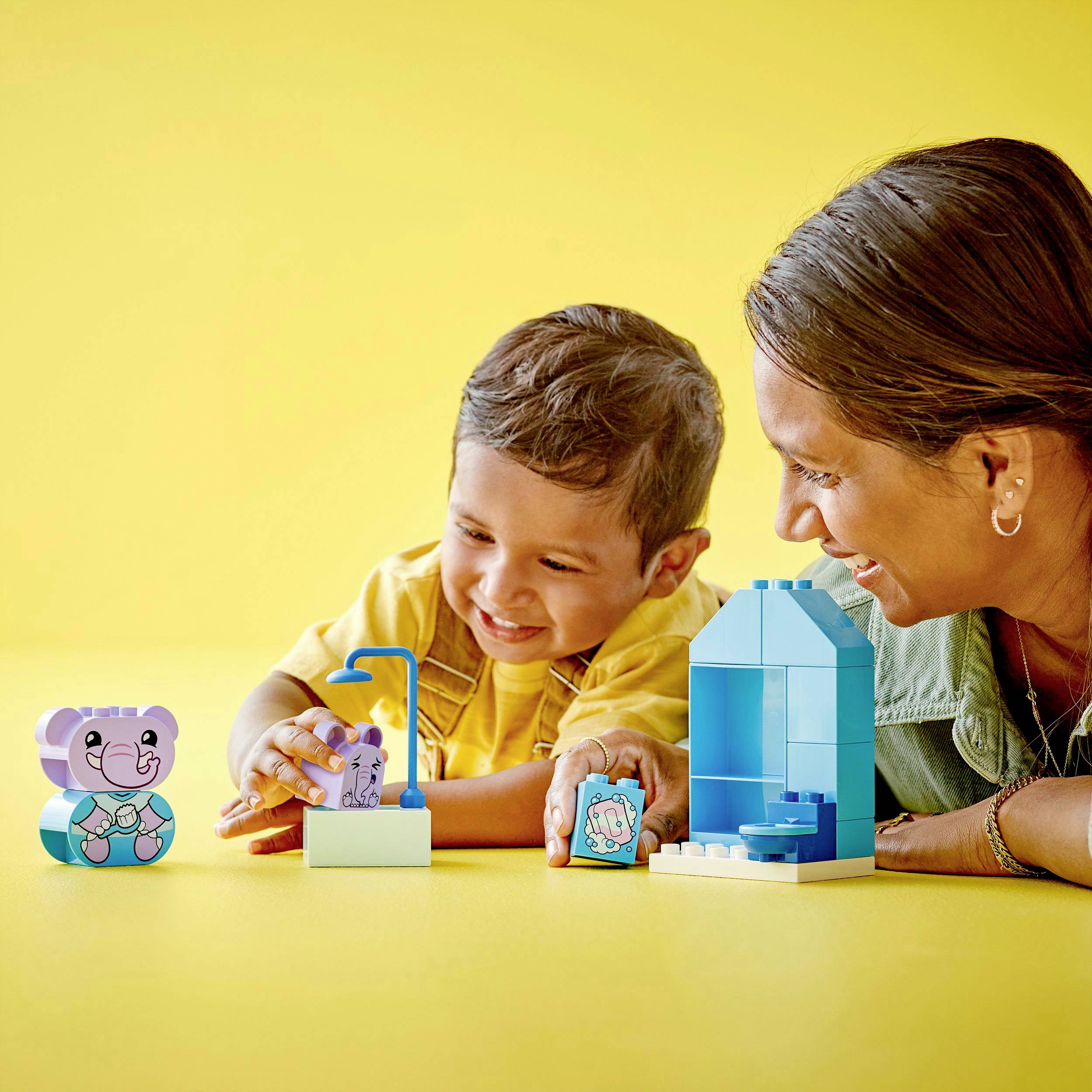 A child smiles and plays with colourful building blocks, while an adult sits nearby and watches. Yellow background.