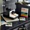 On a table sits a Polaroid camera built from Lego, surrounded by Polaroid photographs and a film package.