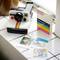 A Polaroid camera and three photographs lie side by side on a table. Next to them sits a box of Polaroid photo film.