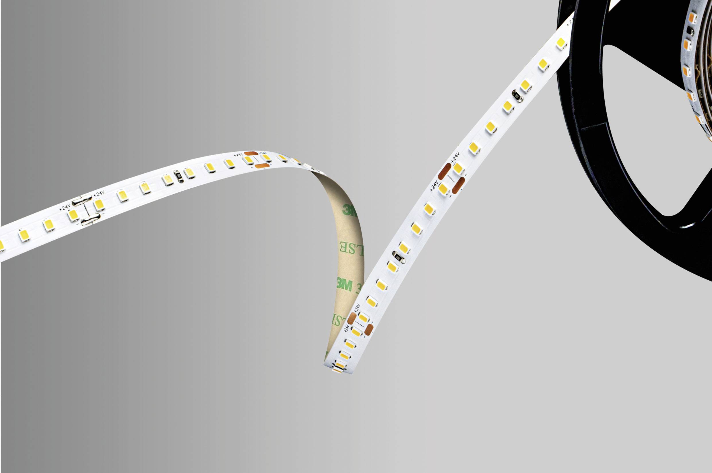 LED strip on a reel, partially unrolled. The strip shows many small, rectangular LEDs and some copper connections.