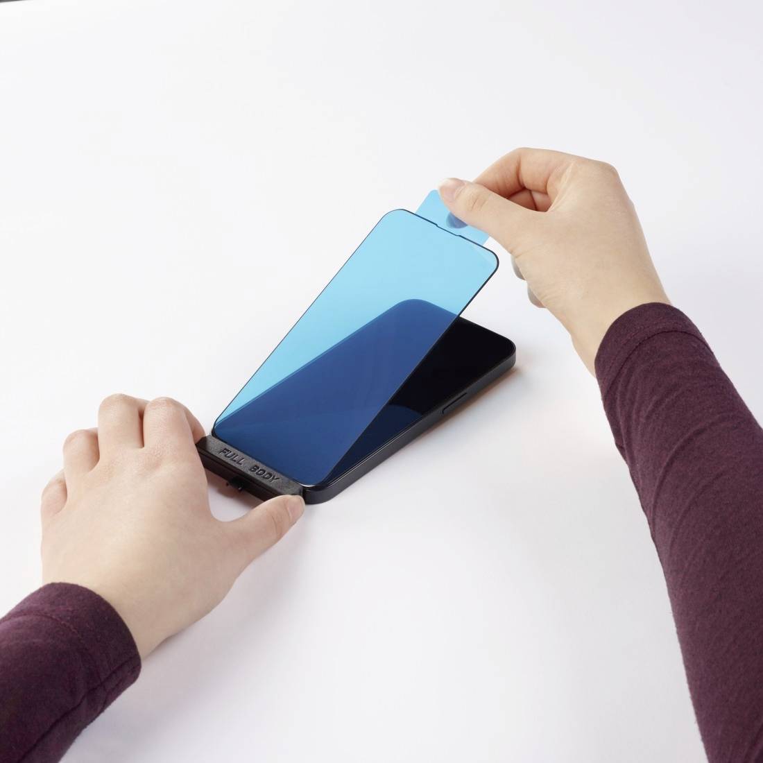 A person is applying a screen protector to a smartphone. The right hand is holding the film, while the left hand is holding the phone steady.