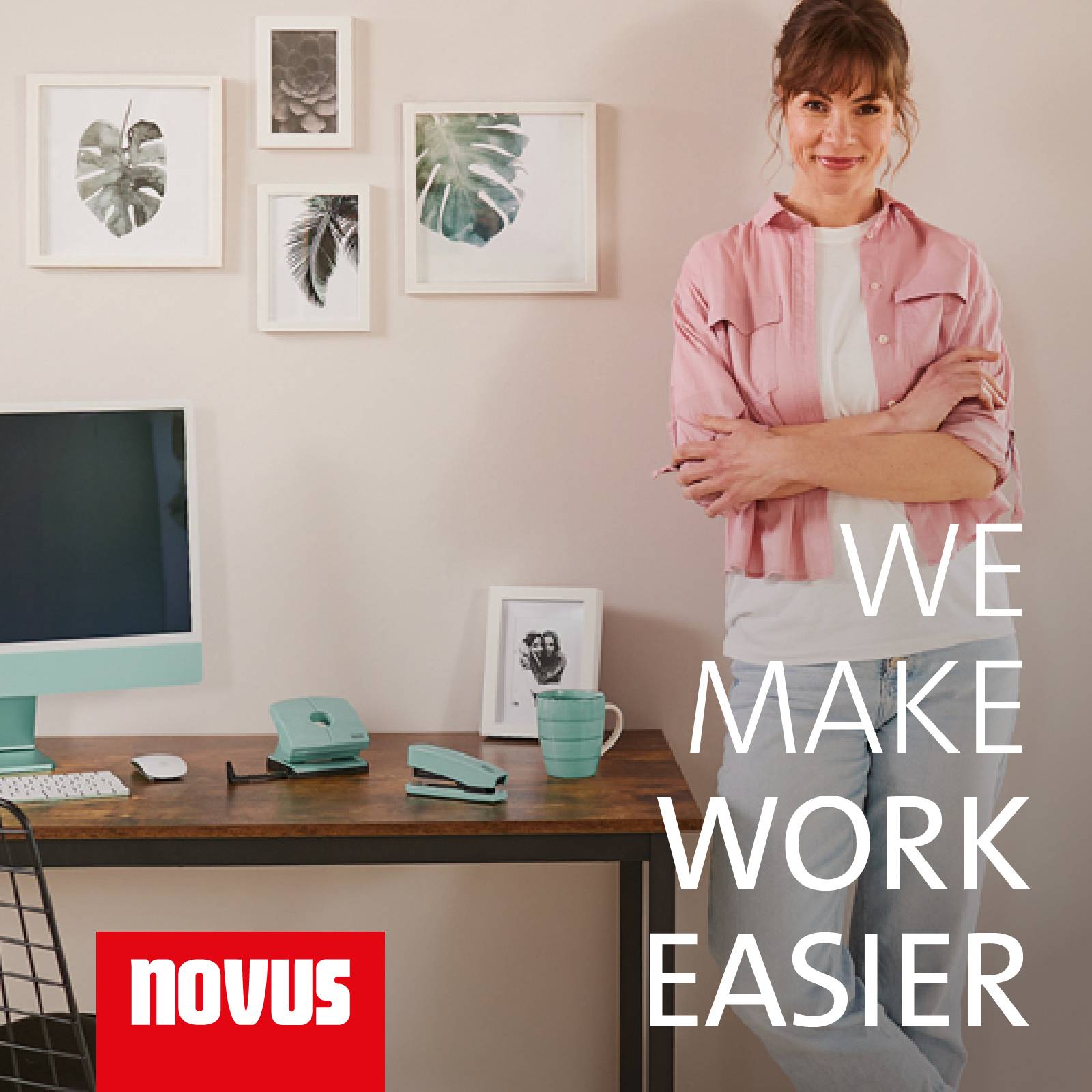 Woman in a pink shirt standing smiling at a desk with a computer monitor, plant pictures on the wall and the slogan 'We make work easier'.