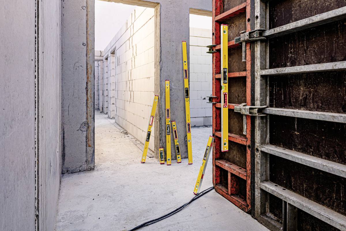 Building under construction with concrete walls. Several spirit levels are leaning against the walls and a scaffolding that is being used for alignment.