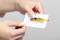 Two hands are holding a plastic bracket with a yellow warning sticker positioned in its centre.