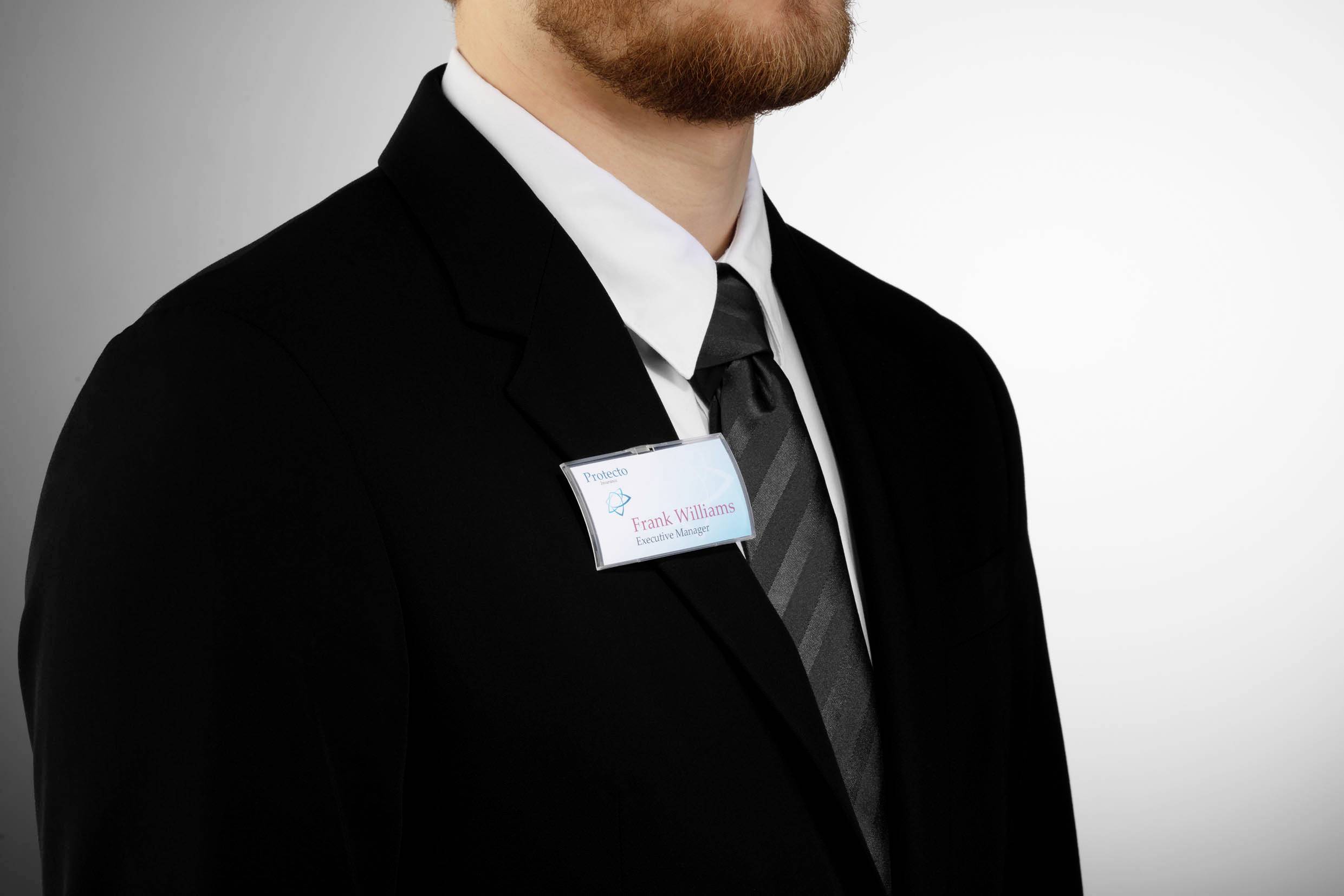 A man in a black suit is wearing a name badge. The background is neutral.