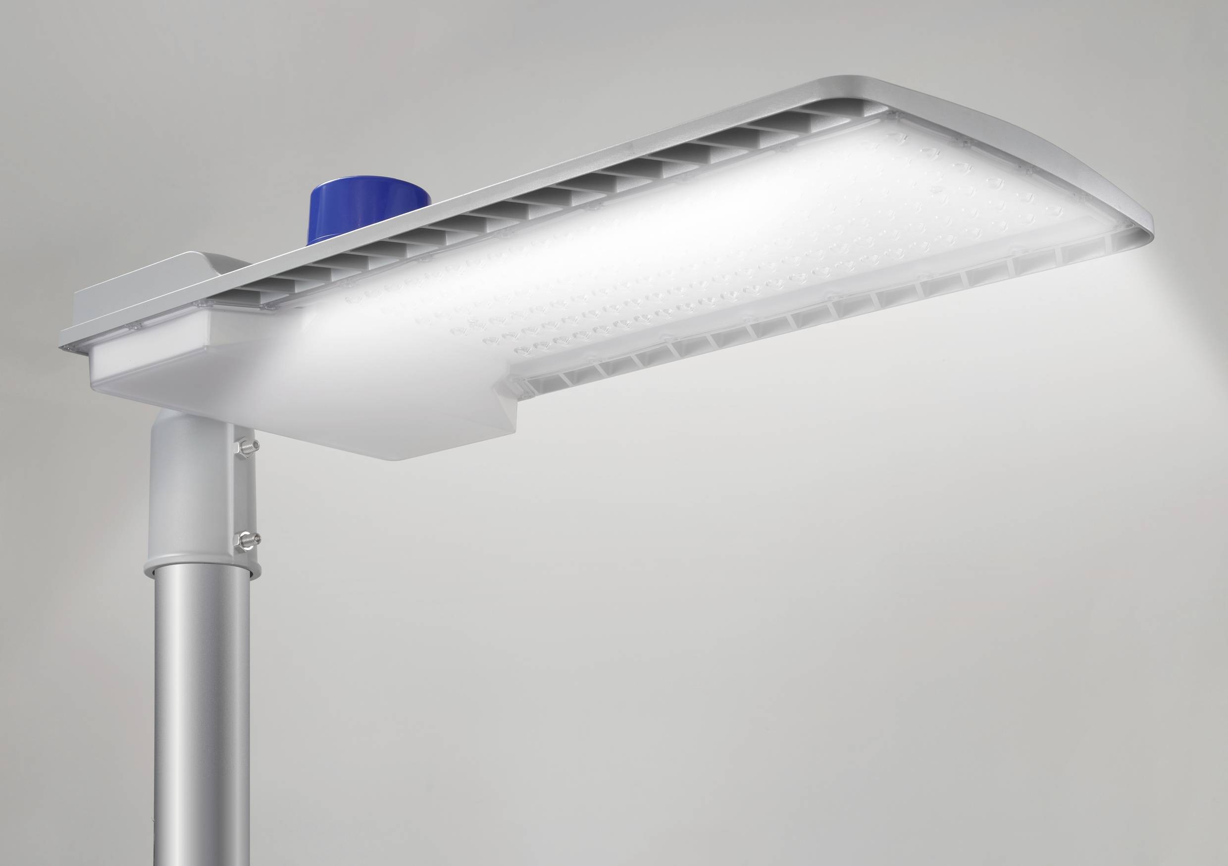 Street lamp with LED light, mounted on a grey metal pole, shining white light downwards.