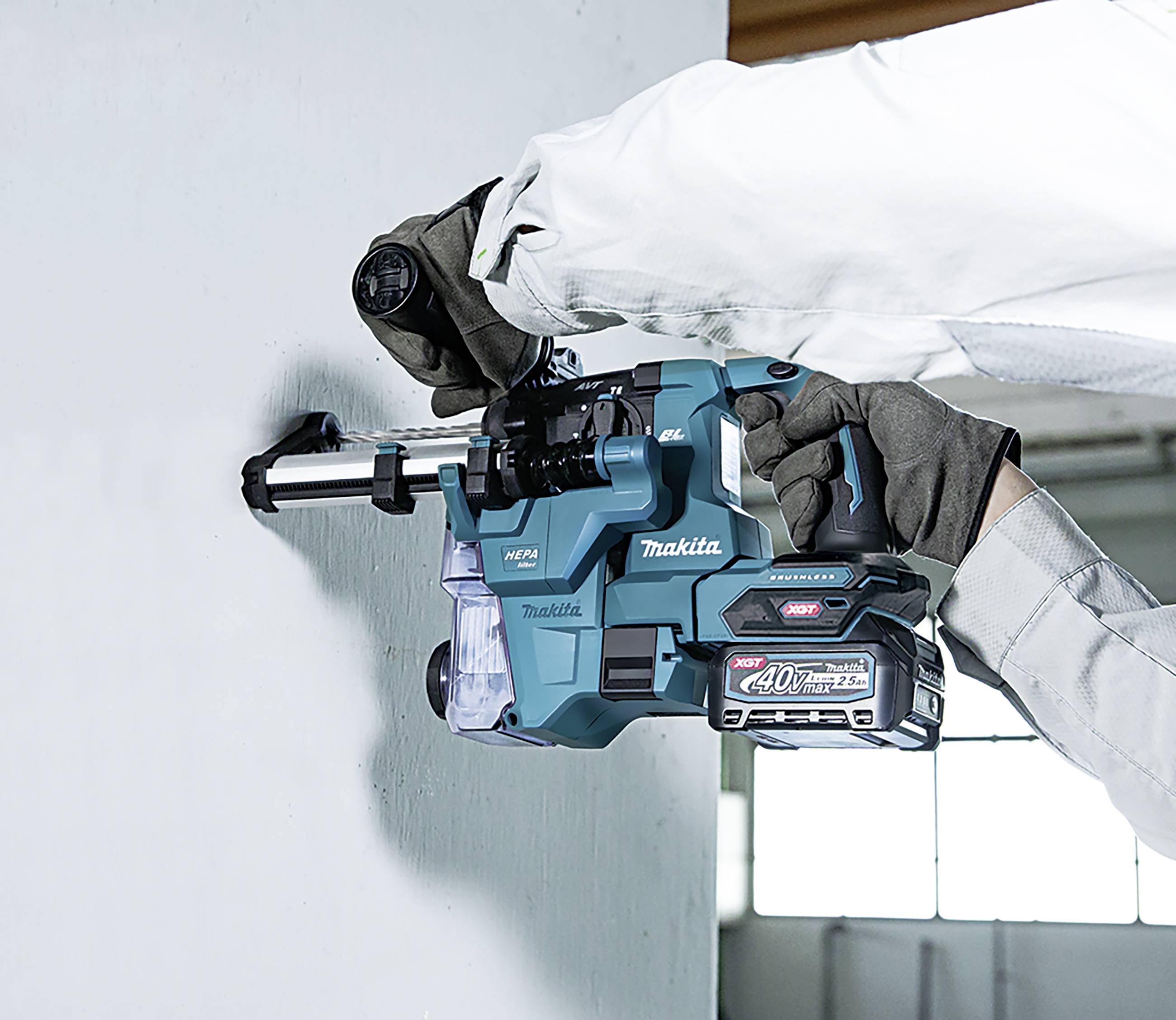 A Makita drill bores into a concrete wall. A worker holds the device securely. The surroundings appear industrial.