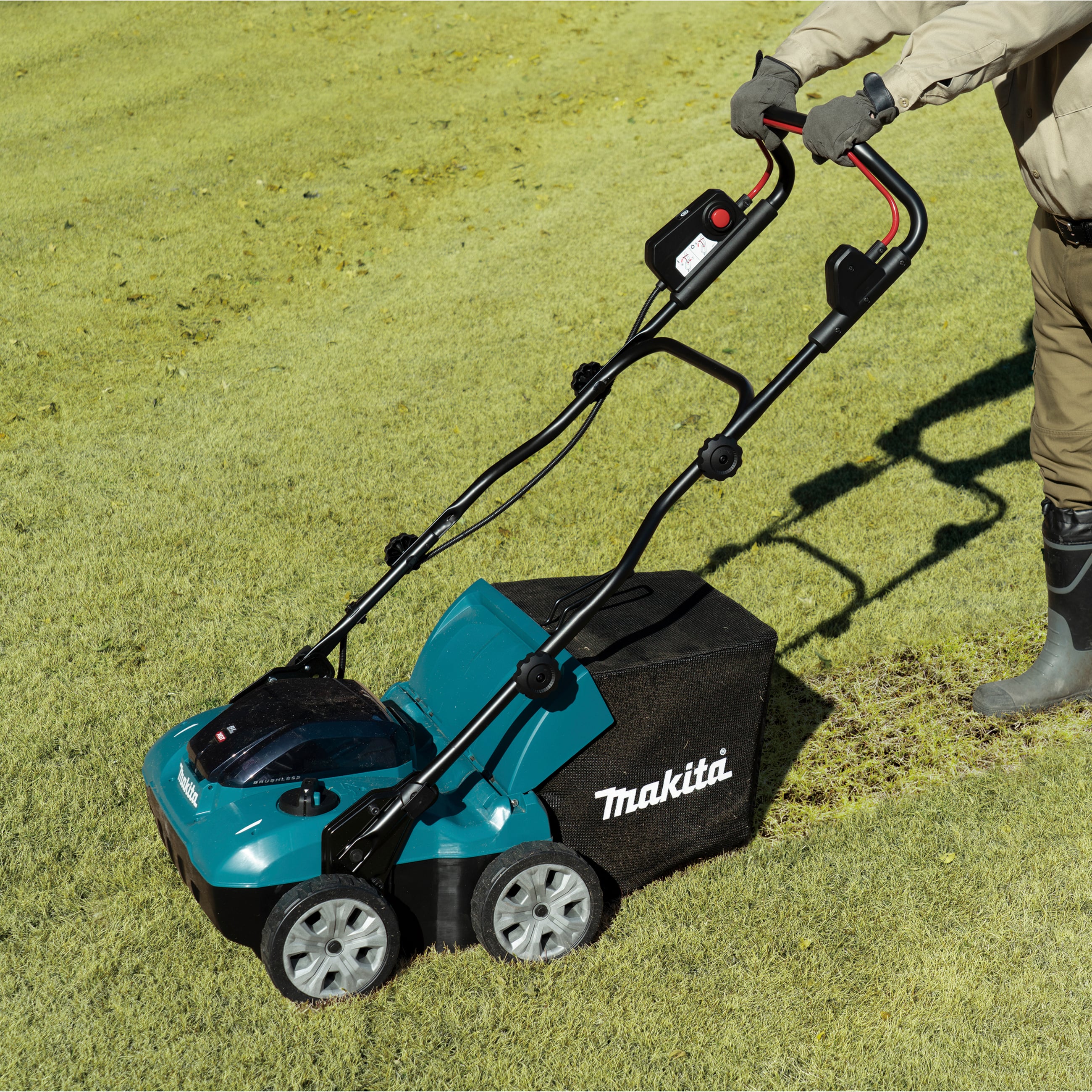 A person is mowing the lawn with a blue lawnmower on a sunny meadow. The 'Makita' logo is visible on the side of the mower.