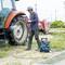 A person is cleaning the large rear tyre of a tractor with a pressure washer in a field.