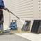 A worker is cleaning black panels on a wall with a high-pressure washer. A blue vacuum cleaner is standing next to it.