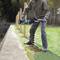 A person is drilling holes into the ground along a path using a blue drill, with trees visible in the background.