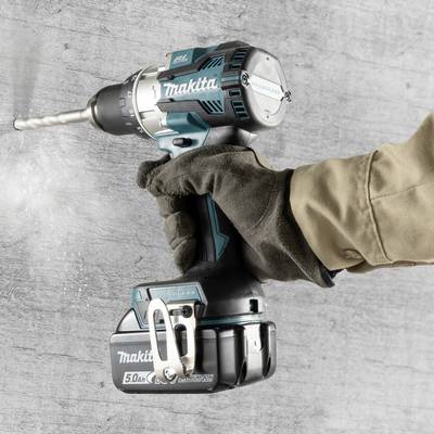 Cordless drill in use, held by a gloved hand, drilling into a concrete wall.