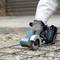 A person is cutting a metal grid with a cordless angle grinder, sparks flying. The machine is turquoise in colour.