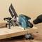 A person is using a mitre saw to cut a wooden board. The saw has a blue protective housing and is being held securely.