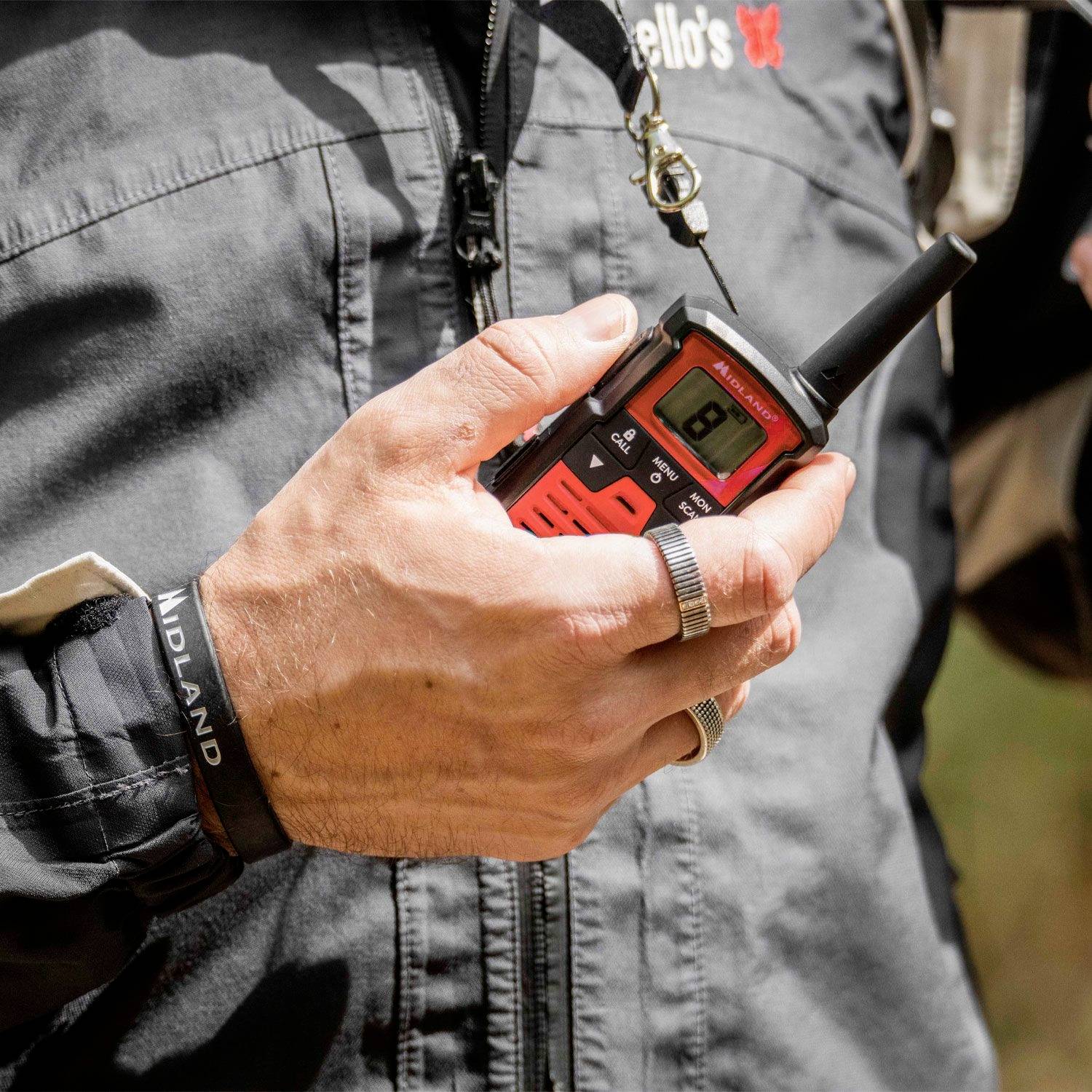 A person is holding a red walkie-talkie in their left hand, ready to communicate. They are wearing a black jacket with a butterfly logo.