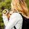 A person is speaking into a yellow walkie-talkie while standing outdoors. They are wearing a rucksack and have long hair.