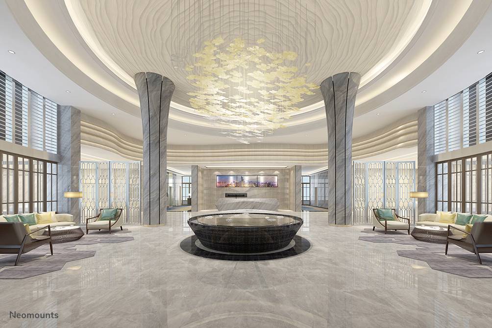 Luxurious hotel lobby with a large, circular table in the centre, modern columns and a magnificent chandelier. Elegant seating areas.