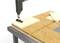 'Power tool drills hole in wooden board on workbench.'
