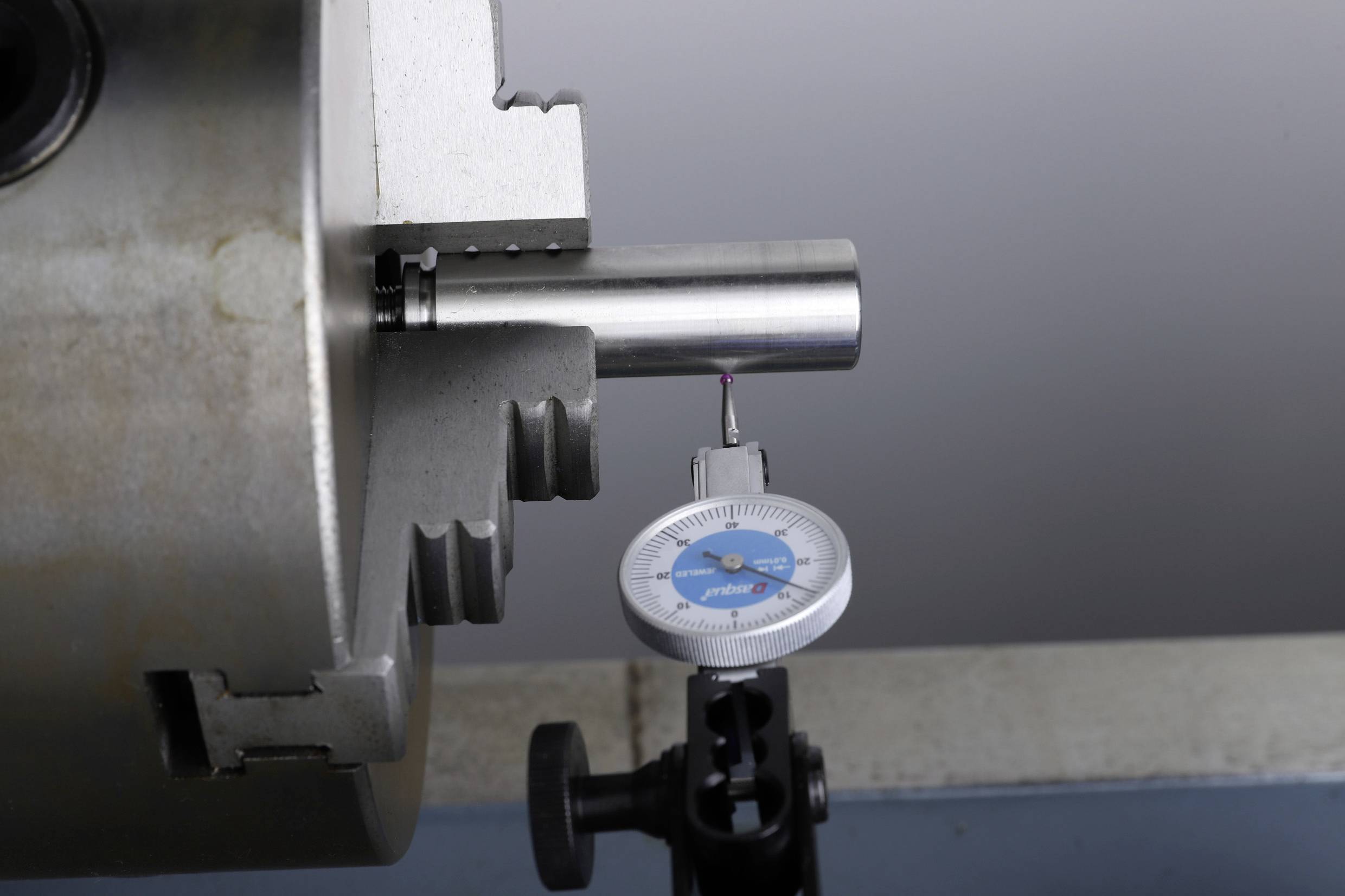 A metal cylinder in a lathe is being checked for run-out with a dial gauge. The needle is indicating on the gauge's scale.