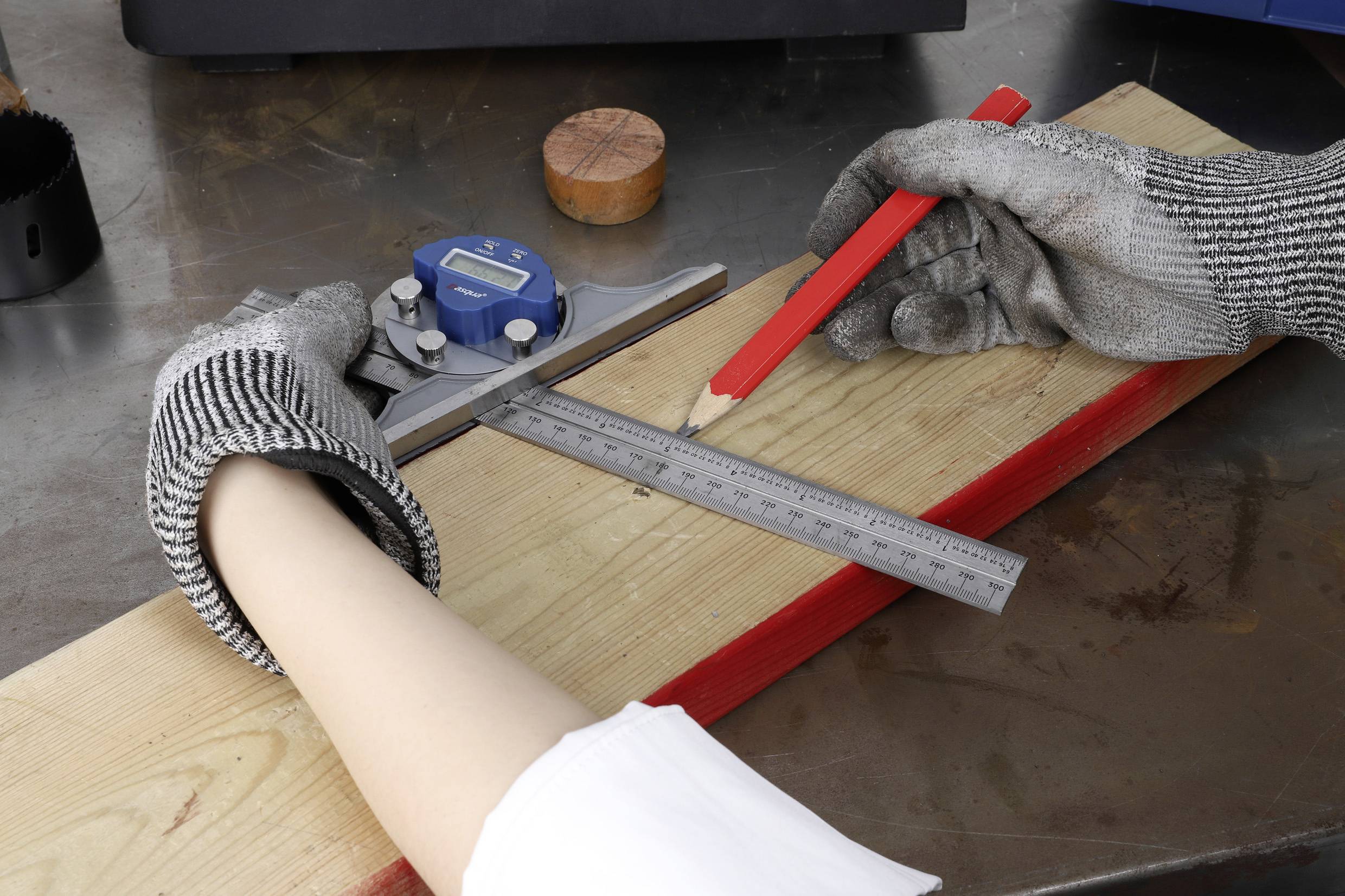 A person wearing gloves is measuring a wooden board with an angle measurer and a ruler, while marking with a pencil.