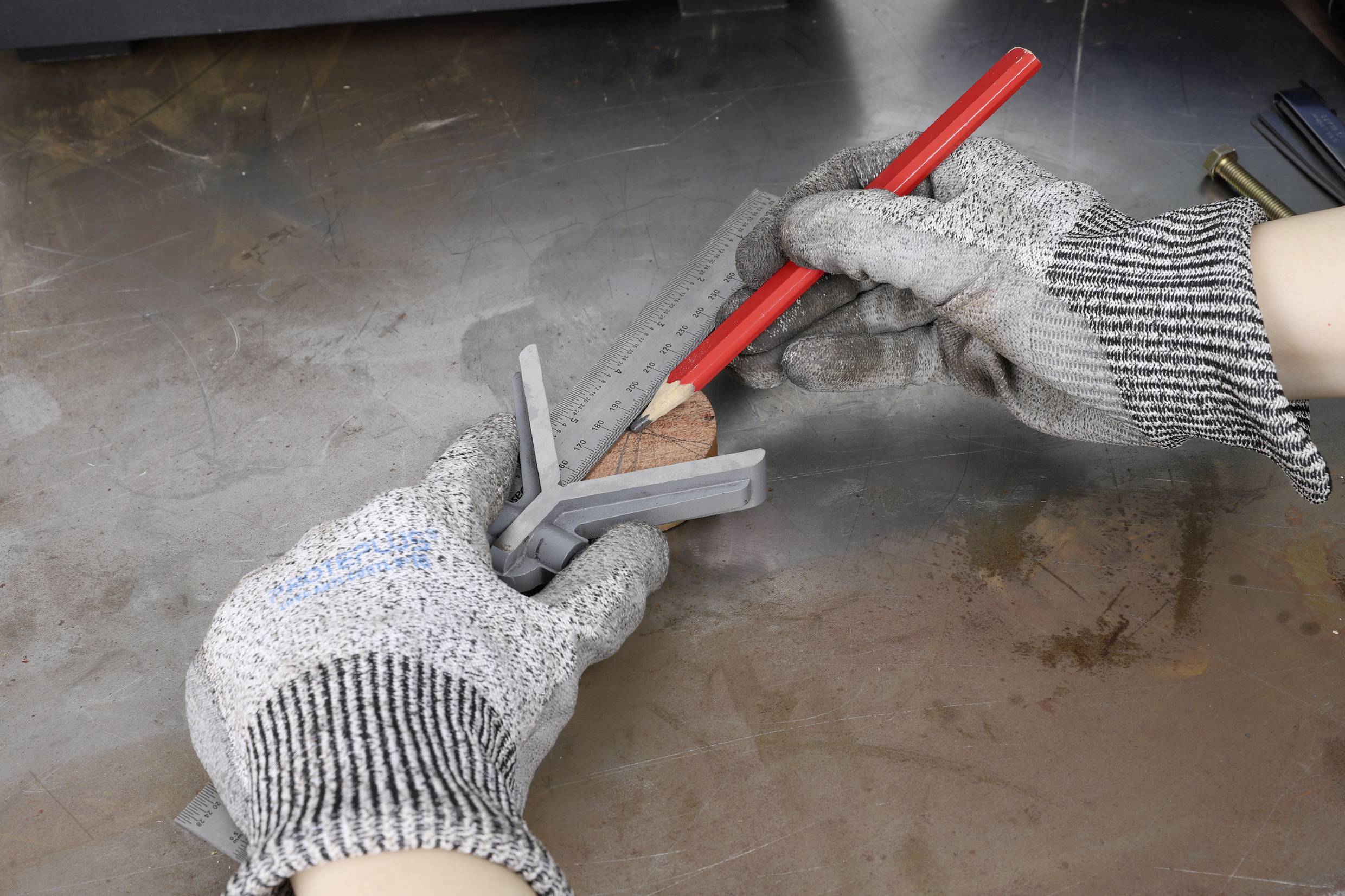 A person wearing work gloves is using an angle gauge and a red pencil to mark a point on a piece of metal.