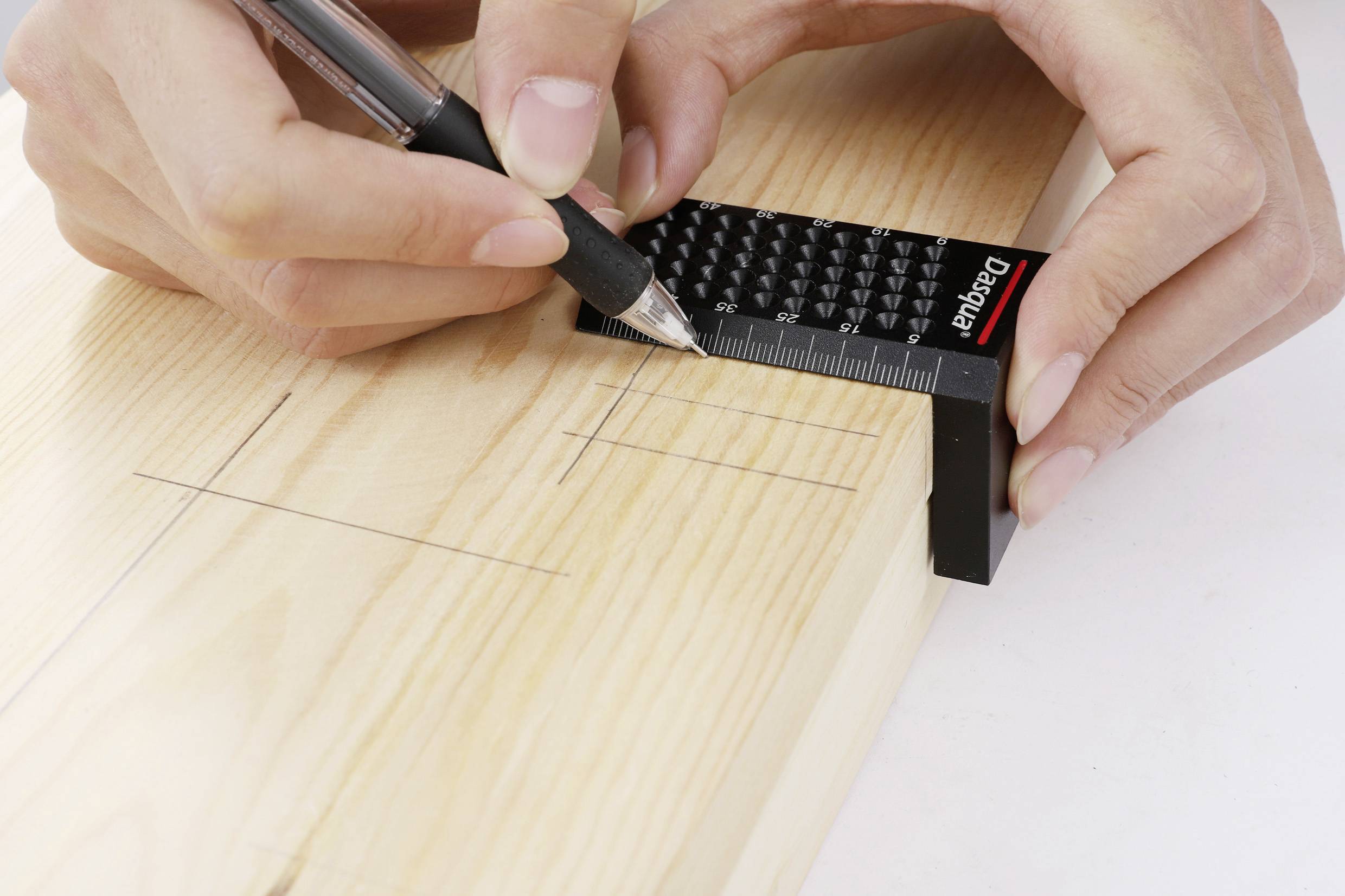 A hand precisely marks lines on a wooden board using a pencil and ruler.