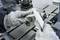 A person wearing grey gloves is measuring a metal piece with a calliper in a workshop environment.