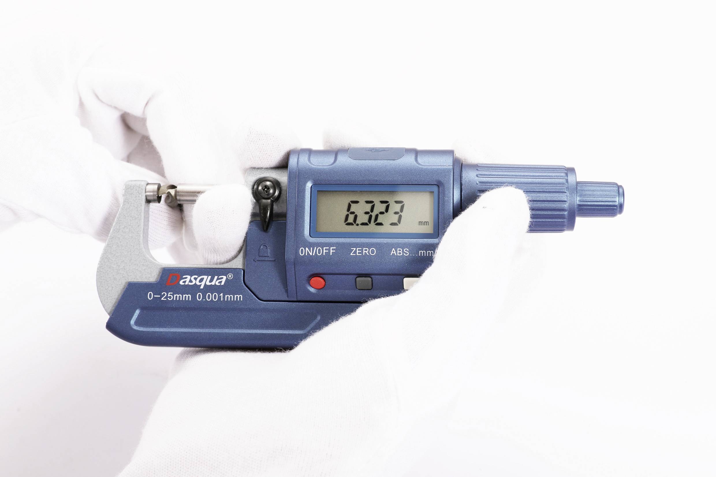 A person is holding a blue micrometer with a digital display showing '6.323'. The instrument is measuring in millimetres.
