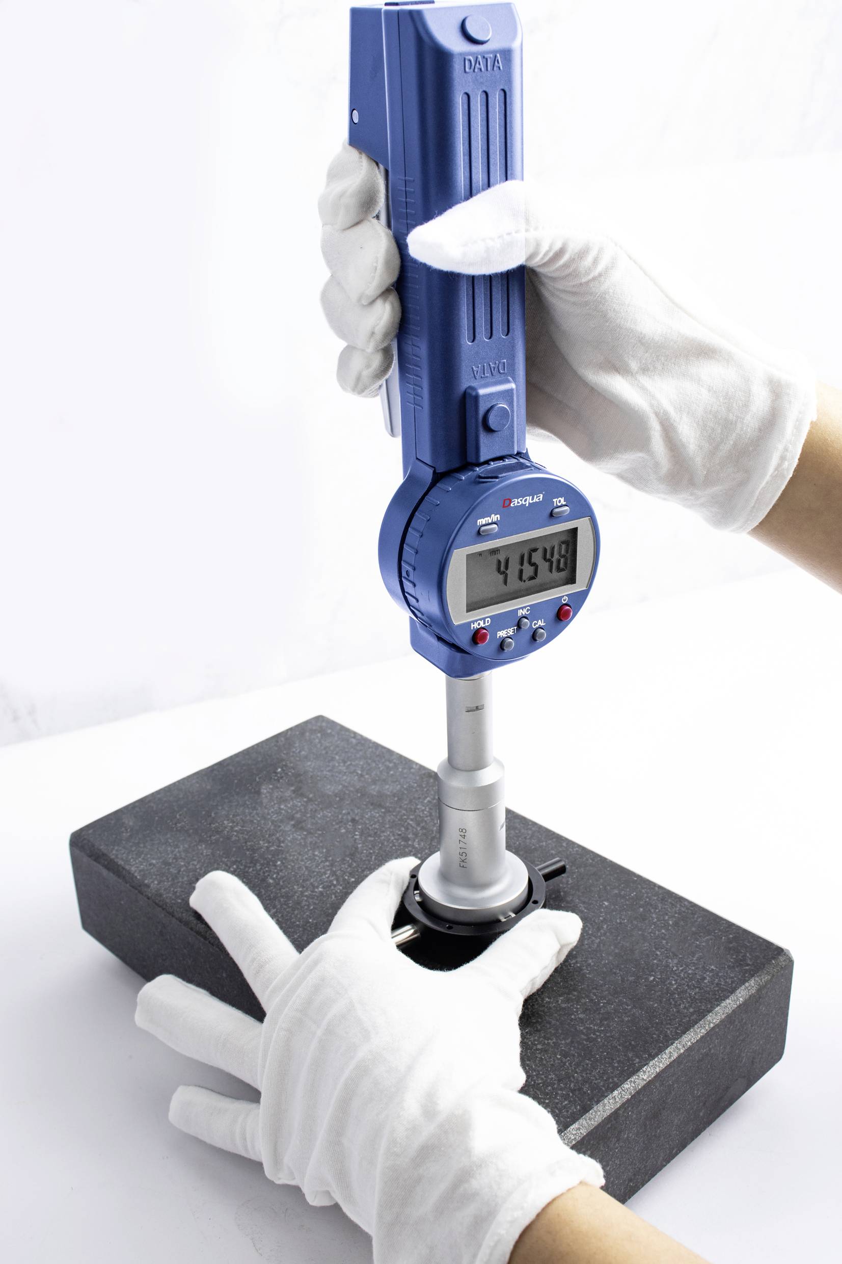 A gloved hand holds a digital measuring device over a black rectangular object. The display shows '41.548'.