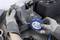 A person wearing gloves is holding a blue adhesive tape next to a metal block on a workbench, surrounded by tools.