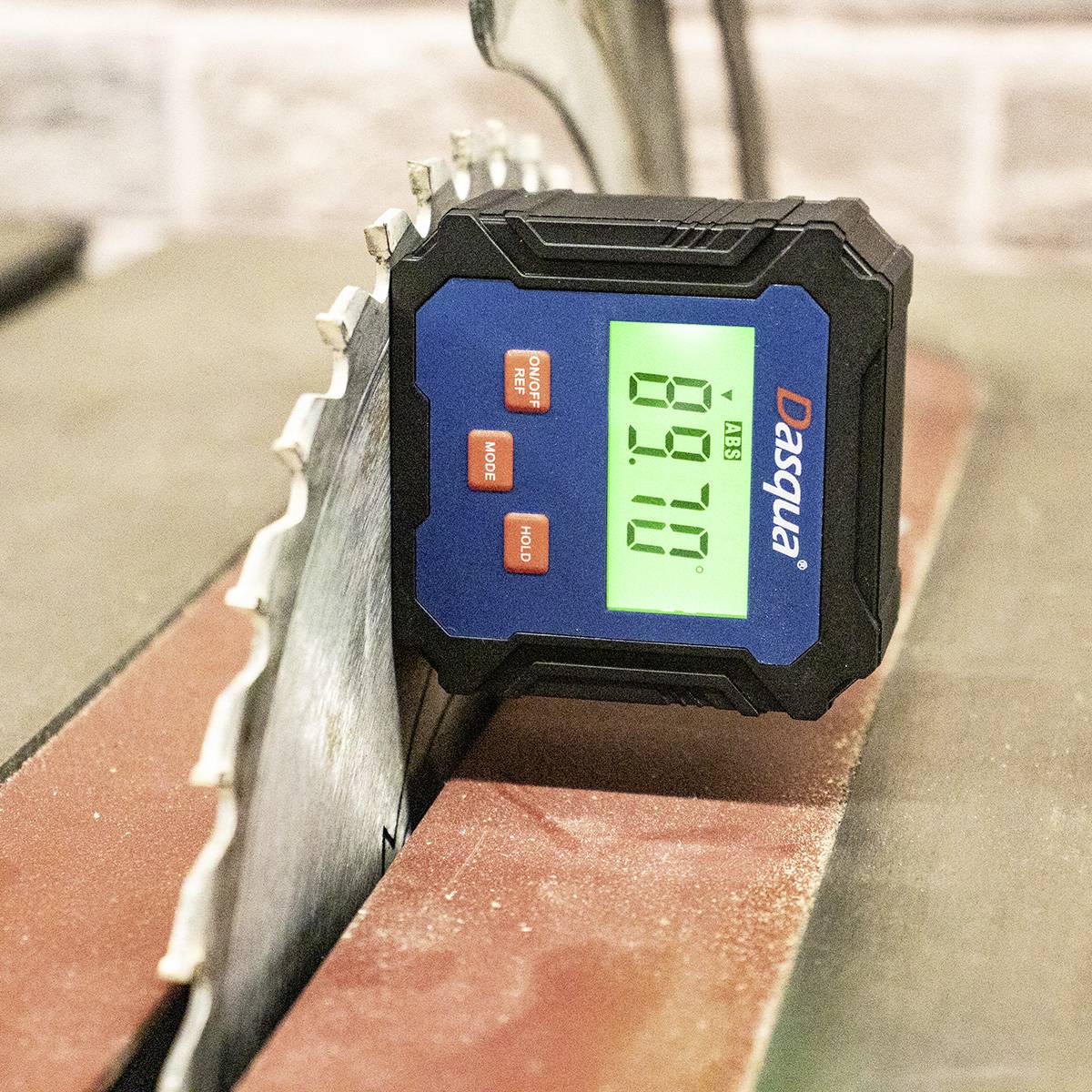 A digital measuring device displays '89.10' on a green screen next to a serrated metal saw on a workbench.