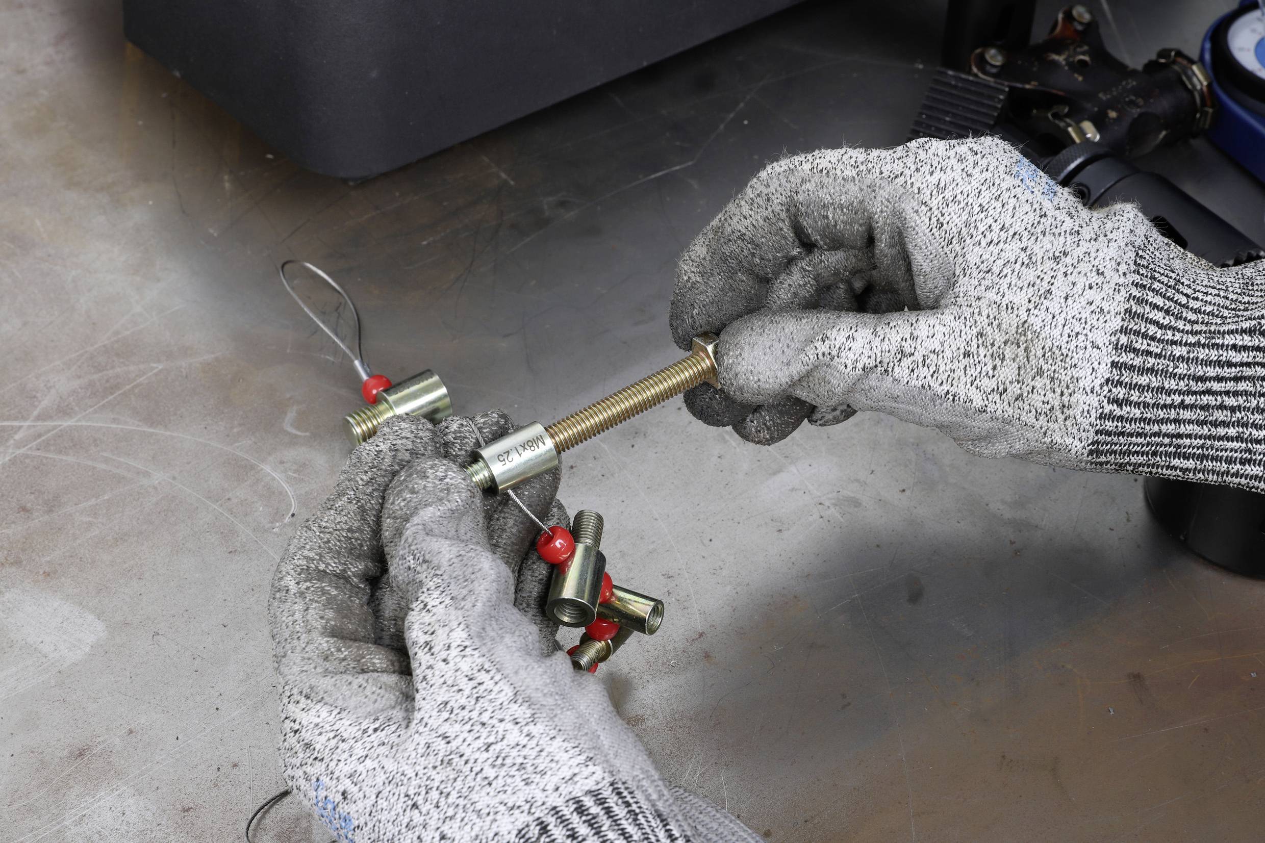 'Two hands wearing work gloves are assembling a heavy component using screws and cables on a workbench.'