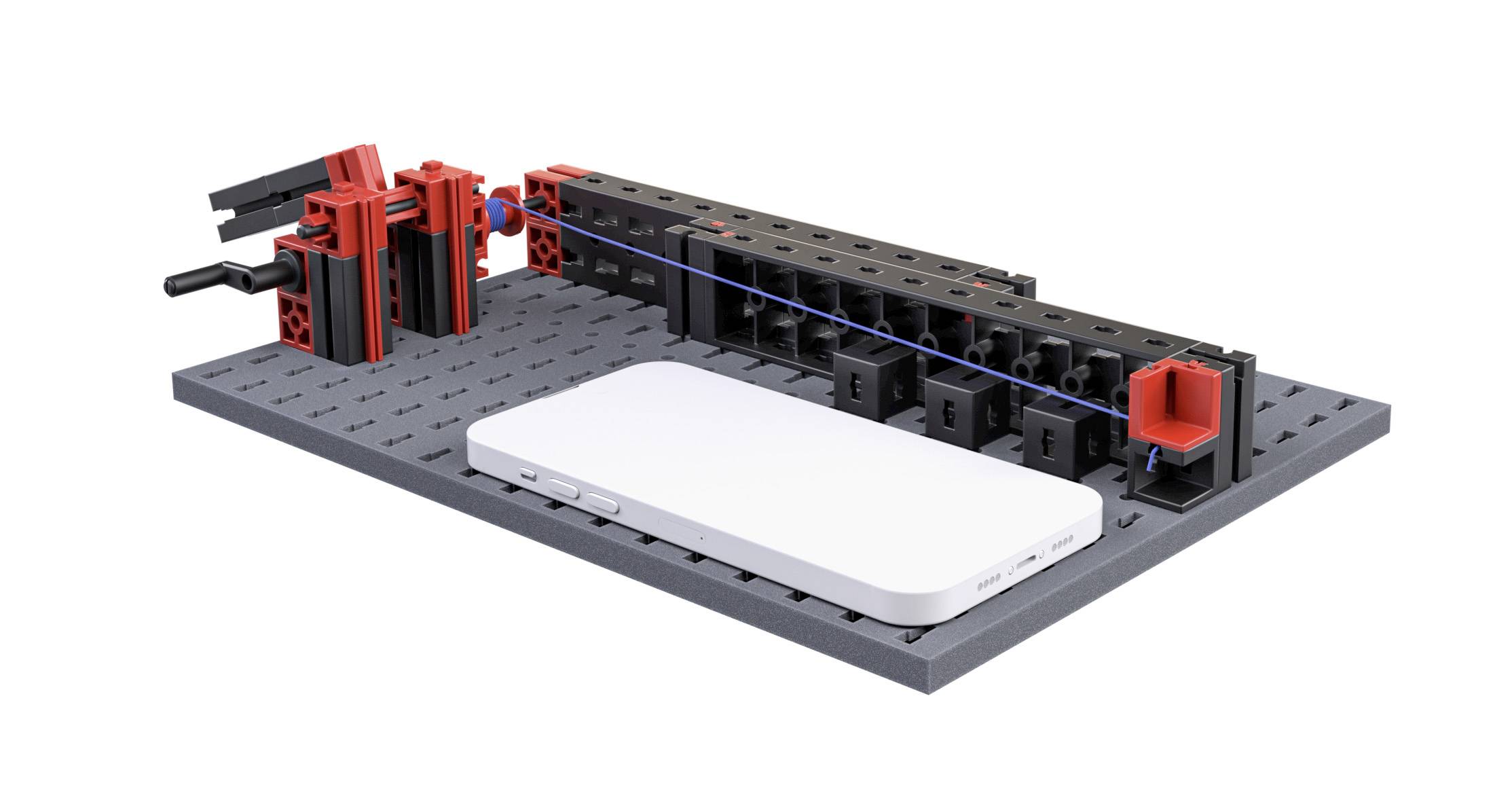 A white smartphone is lying on a black case with red and black components, part of a technical model or experiment.