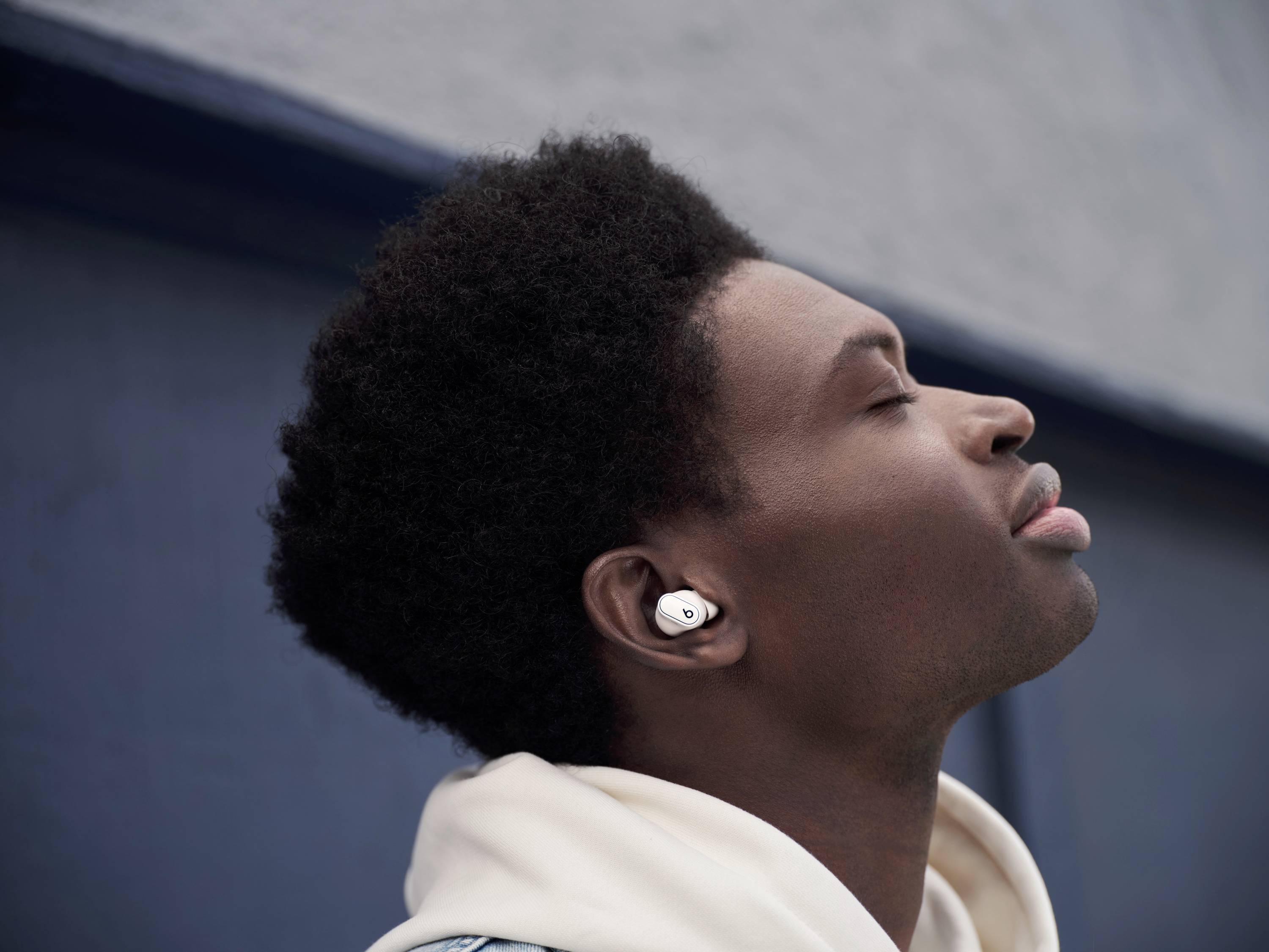 A person wearing headphones relaxes outdoors, eyes closed, against a grey background.