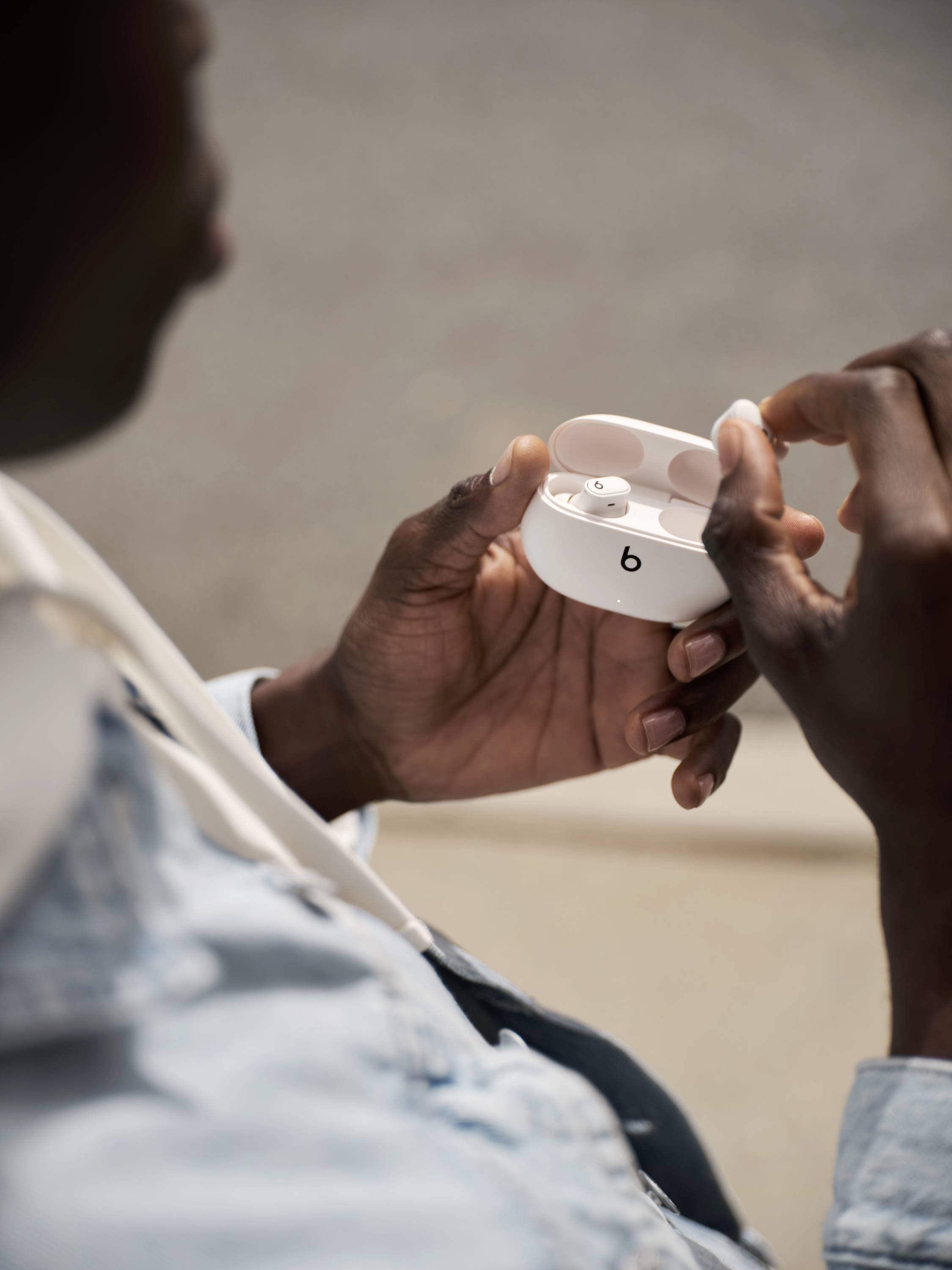 A person is holding an open charging case with wireless in-ear headphones. The headphones have a simple, modern design.