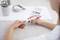 A person is using an electric manicure tool on their fingernail. Cotton pads and nail decorations are lying in the background.