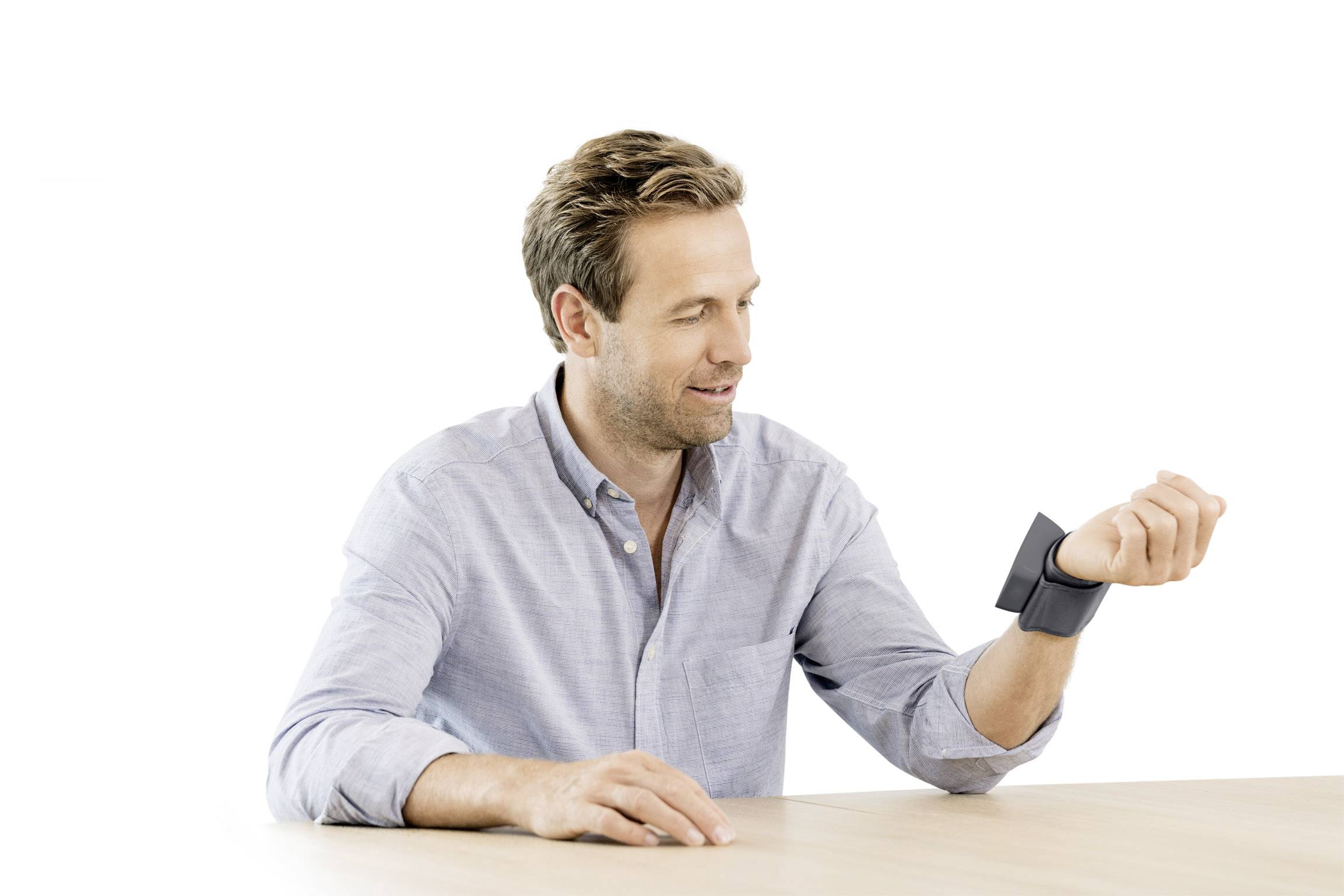 A man is measuring his blood pressure with a digital wrist blood pressure monitor at the table.