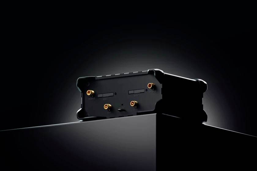 A black electronic device with metal ports stands in focus on a dark surface against a black background.