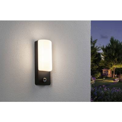 A modern exterior wall light with a rectangular white shade illuminates a wall at dusk. In the background, a garden can be seen.