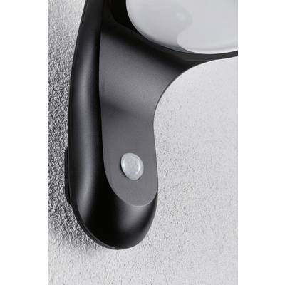 Close-up of a black motion sensor mounted on the wall with a circular light sensor at the top. Background of a grey textured wall.