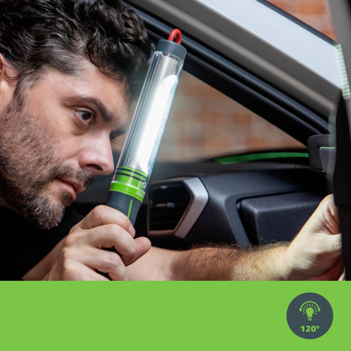 A man is checking the interior of a car with a bright torch. In the foreground, a green field with a lightbulb symbol.