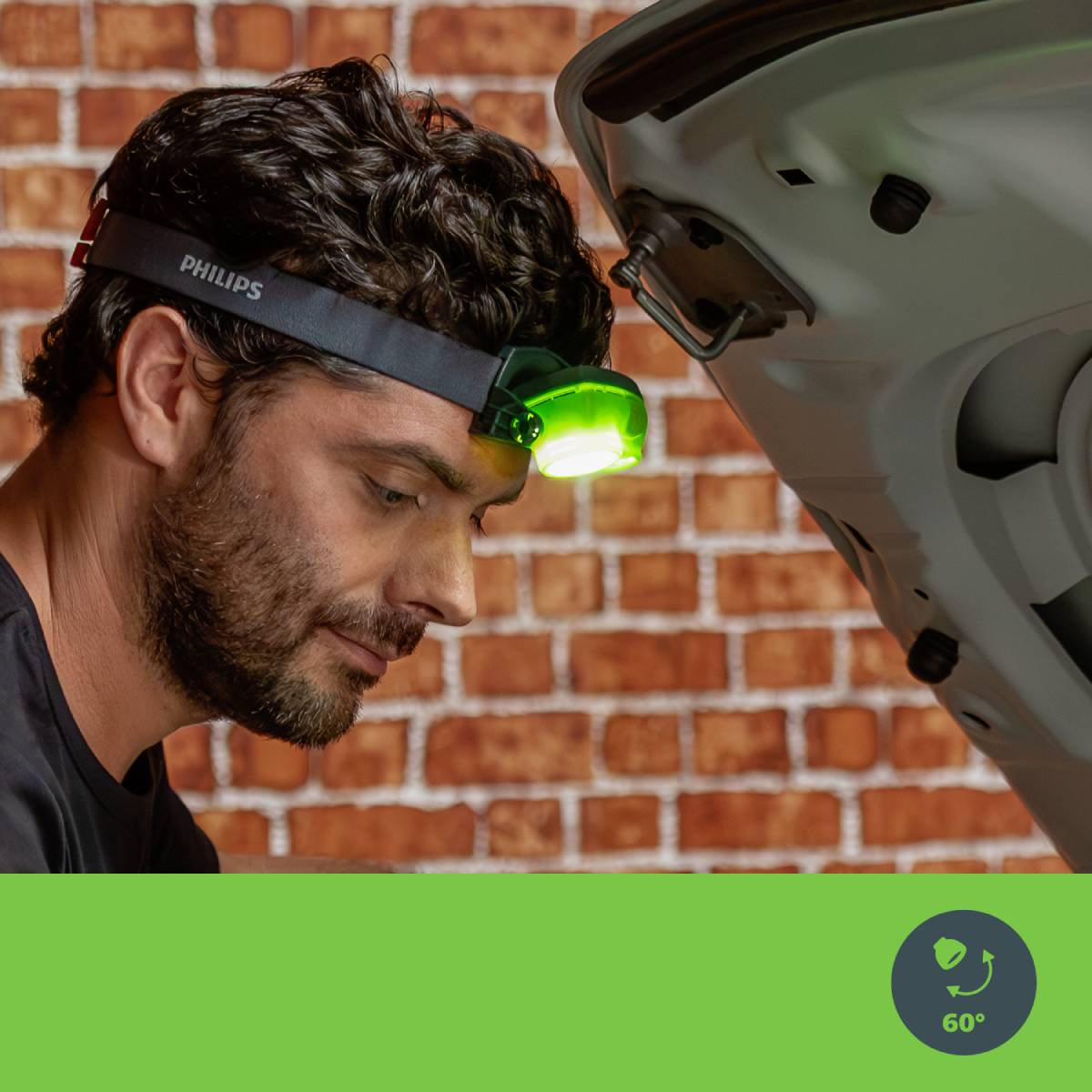 A man is wearing a head torch and looking into the engine compartment of a car. A brick wall is in the background. In the bottom right, there is a symbol with a heart and the number 60°.