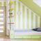 A children's bedroom with green and white striped walls, a bed with storage, a wall clock, and a shelf with plants.