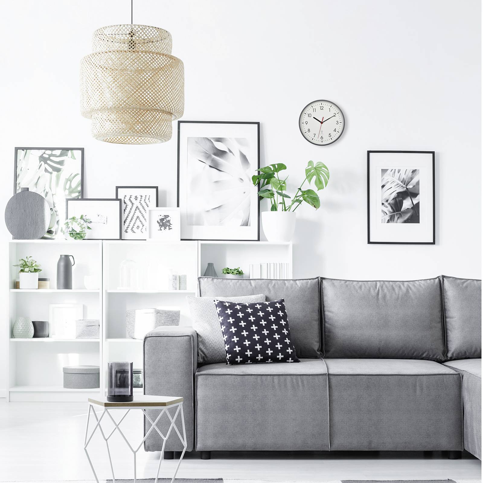 A modern living room with a grey sofa, decorative cushions, a white shelving unit with plants and picture frames on the white wall.