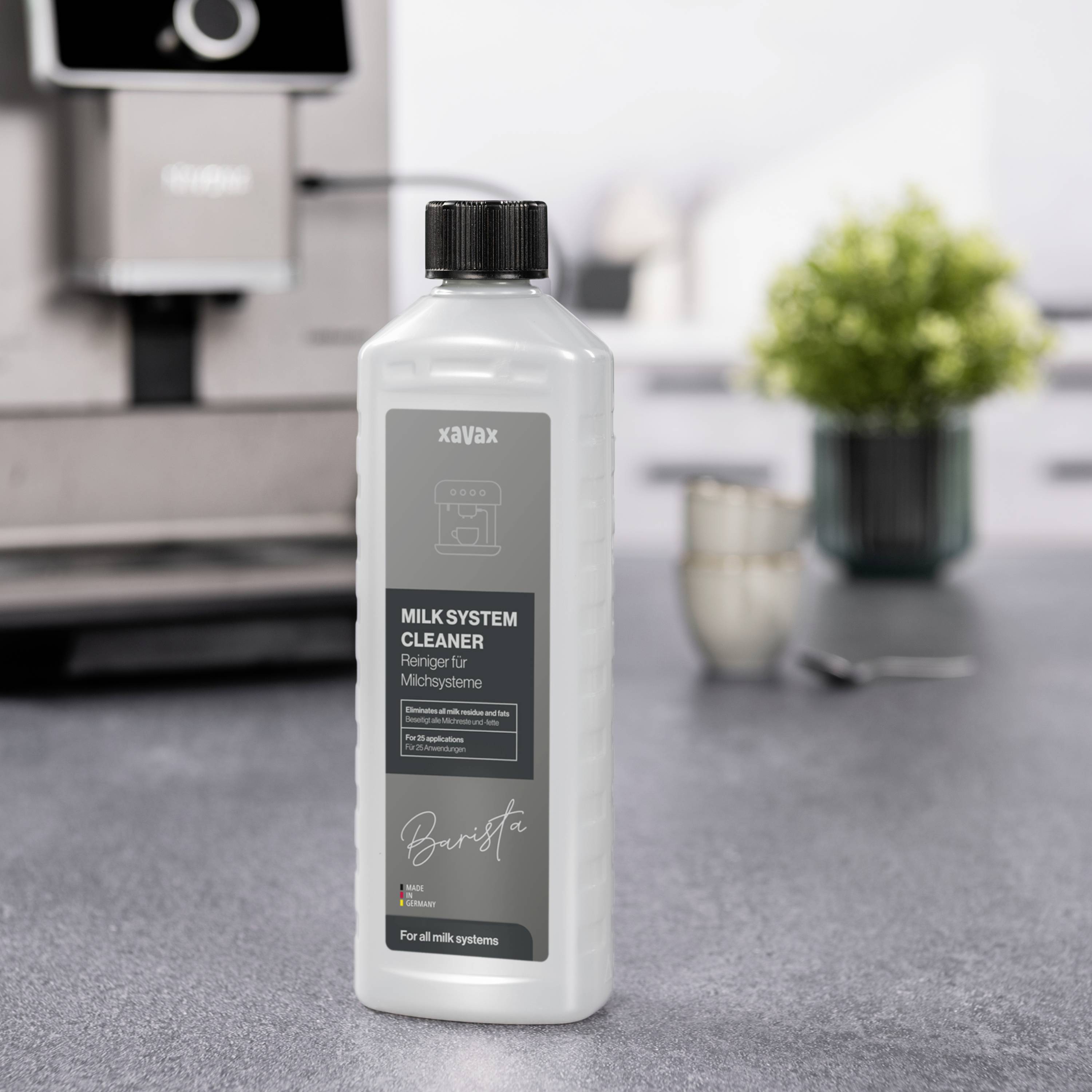 'Milk System Cleaner' bottle in the foreground in front of a coffee machine on a worktop.