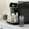 Black coffee machine with display sits on kitchen worktop. Next to it is a packet of cleaning tablets and a white mug. In the background, a biscuit jar and milk.