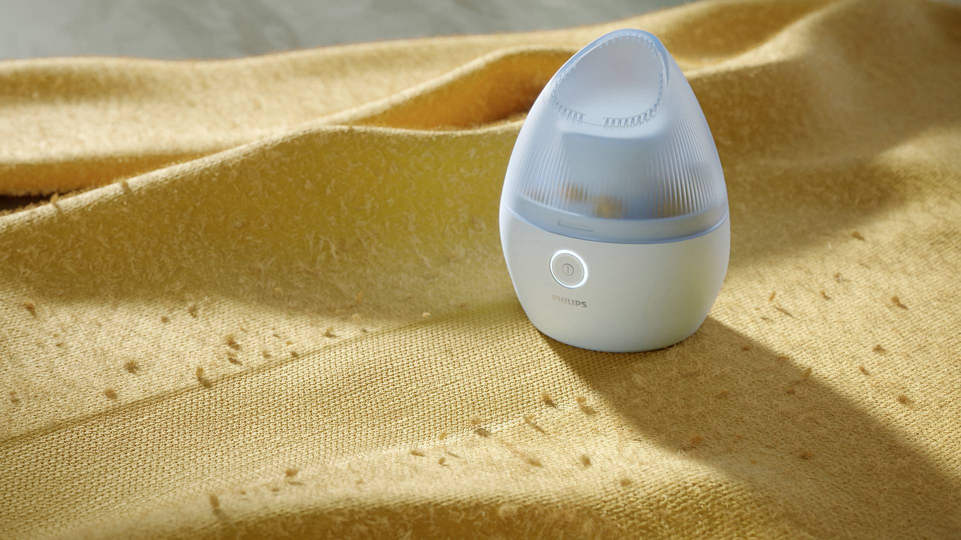 An oval, blue humidifier sits on a golden cloth. The lighting emphasises the soft texture of the fabric.