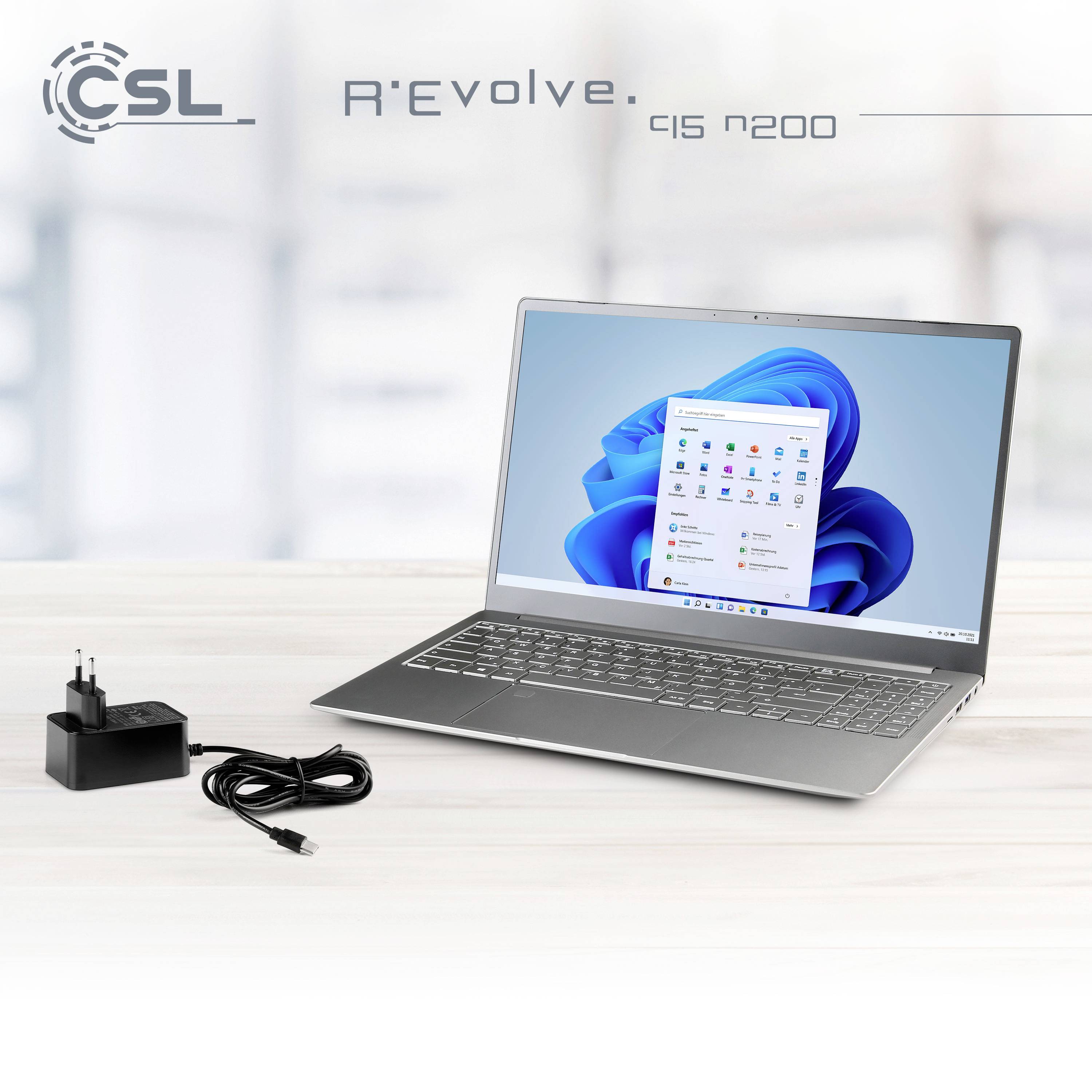A silver laptop on a table with a power adapter beside it. The screen displays a blue and white user interface.