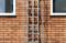 A metal ladder is fixed to a brick wall and leads upwards between two windows.